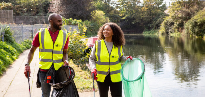 Man and woman in hi-vis jackets walking along canal litter pick