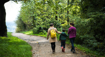 Two women and child walking away from camera along woodland footpath in Surrey Hills AONB