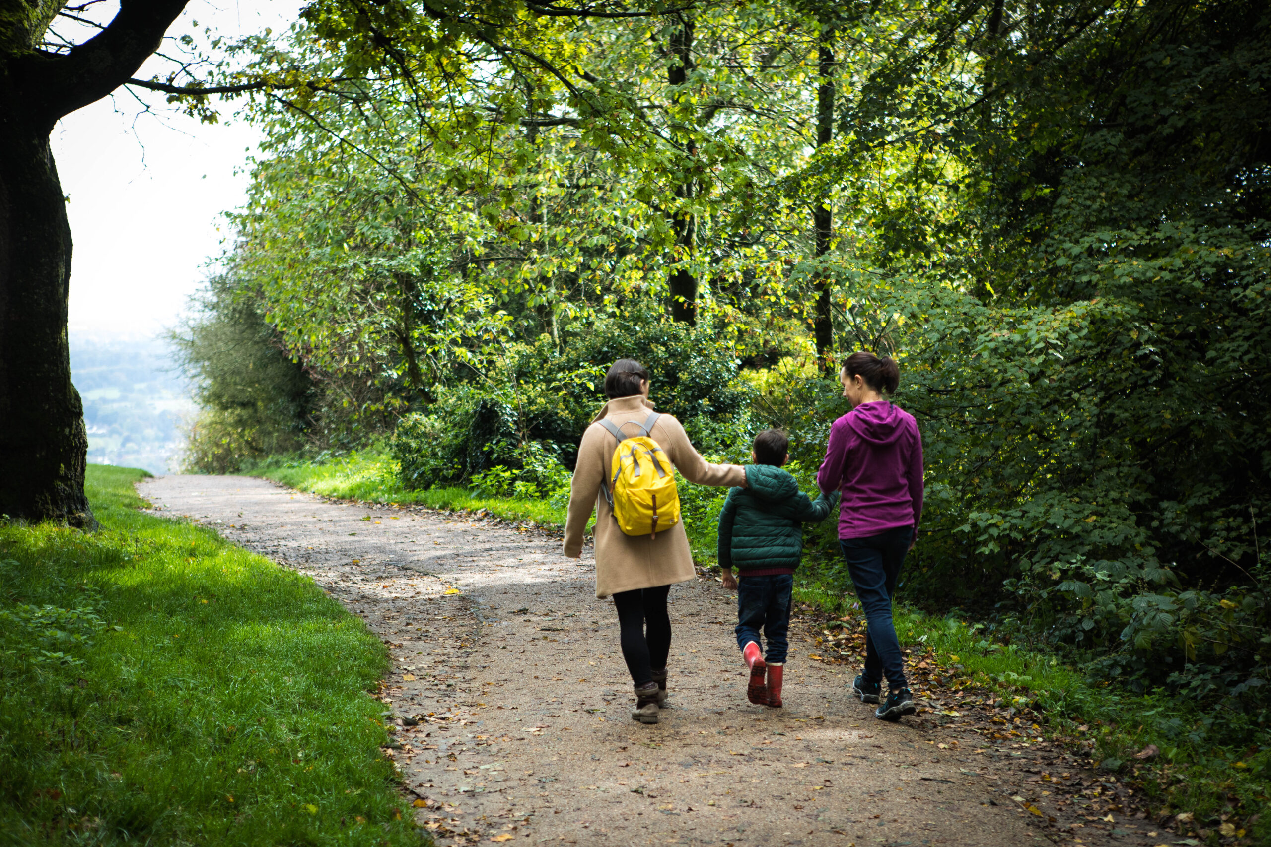 Two women and child walking away from camera along woodland footpath in Surrey Hills AONB